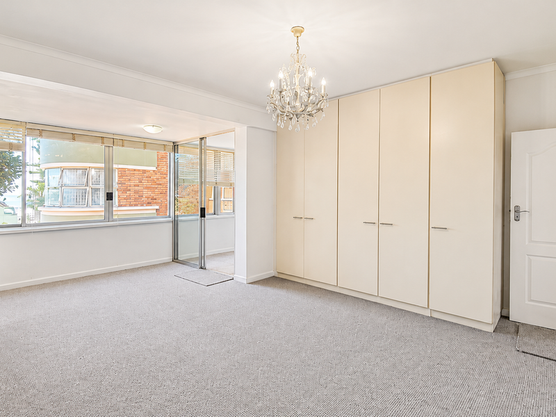 Spacious bedroom featuring neutral carpeting, extensive built-in storage cupboards, a decorative chandelier, and large windows providing natural light.