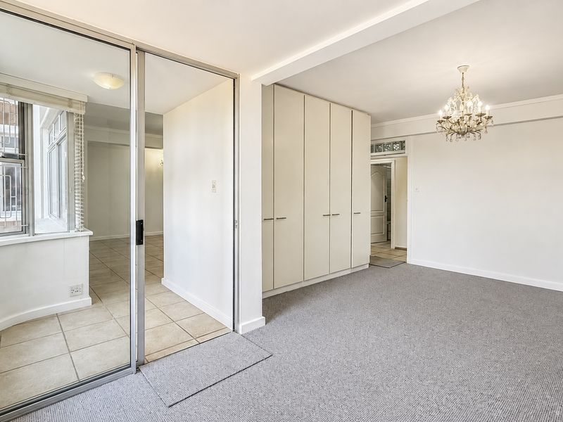 Spacious living area featuring neutral carpeting, built-in storage cupboards, and a glass-enclosed sunroom or balcony space with tiled flooring.