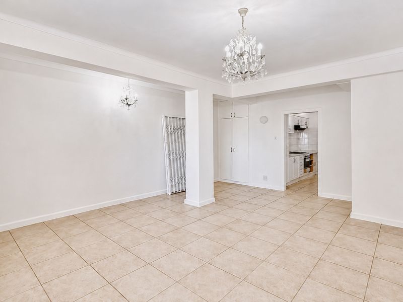 Spacious open-plan living area featuring neutral tiled flooring, elegant crystal chandeliers, and built-in storage, with a clear view into the adjacent kitchen.