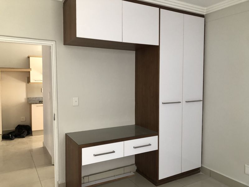 A clean bedroom featuring a modern built-in wardrobe with an integrated desk unit, neutral wall finishes, and tiled flooring.