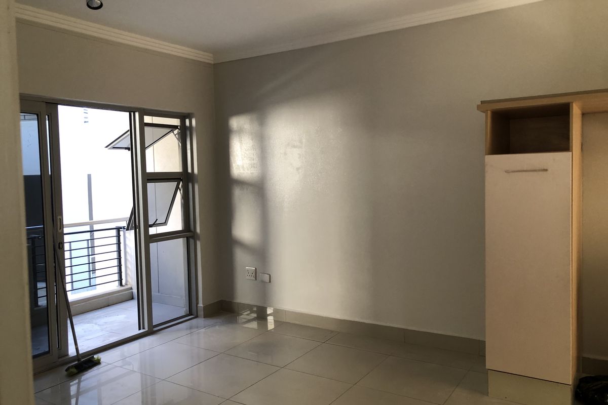 A bright, empty bedroom featuring tiled flooring, a built-in cupboard, and a sliding glass door providing access to a balcony.