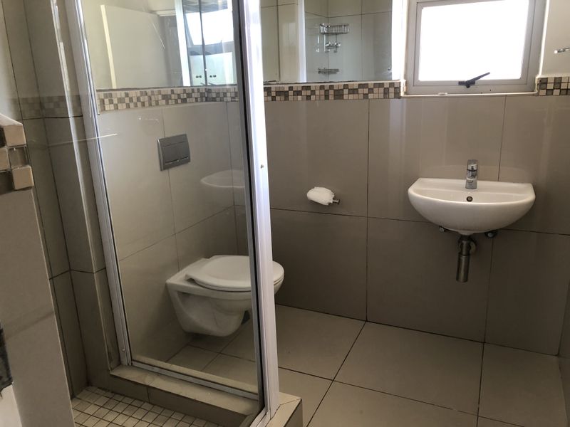 A clean, modern bathroom featuring a wall-mounted toilet, wall-mounted basin, and a glass-enclosed shower with neutral tiled finishes.