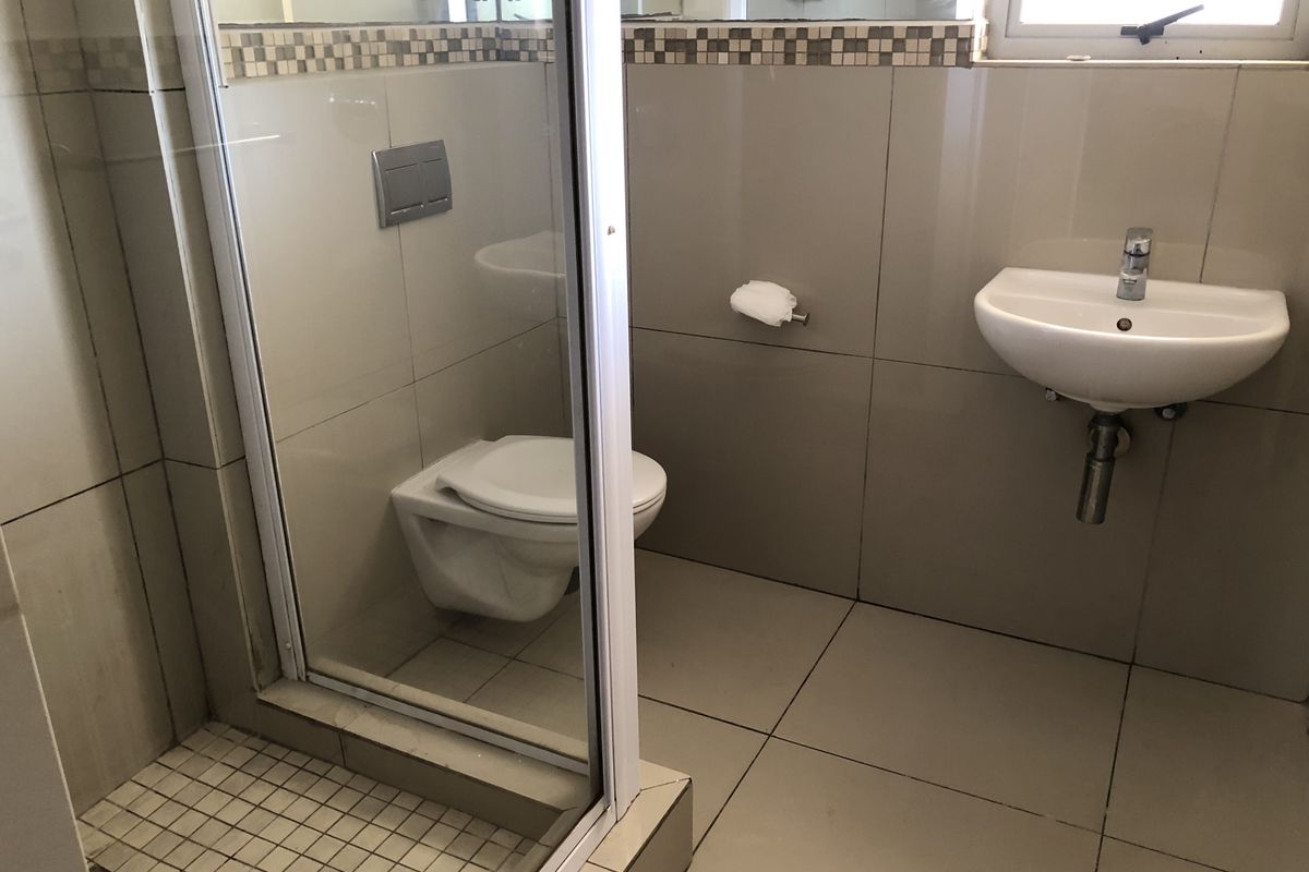 A clean, modern bathroom featuring a wall-mounted toilet, a glass-enclosed shower, and a wall-mounted basin with neutral ceramic tiling.
