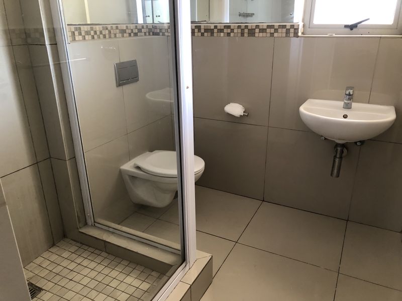 A clean, modern bathroom featuring a wall-mounted toilet, a glass-enclosed shower, and a wall-mounted basin with neutral ceramic tiling.
