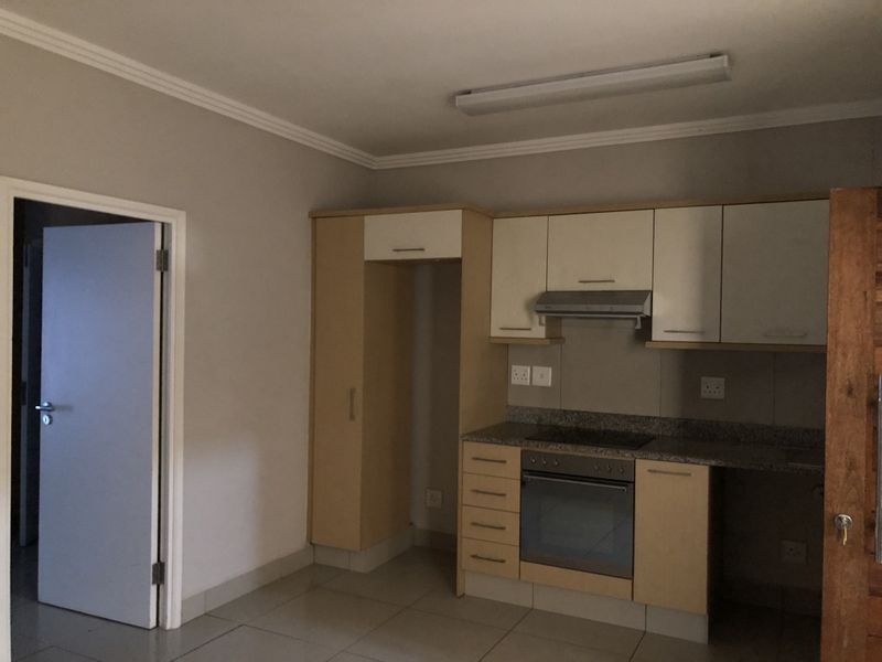 A functional kitchen featuring built-in cabinetry, stone countertops, an integrated oven, and an extractor fan, with neutral tiled flooring and coving.