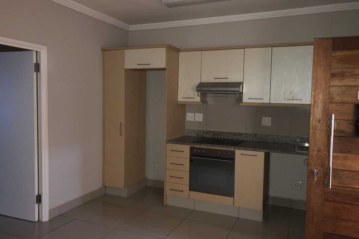 A compact kitchen featuring built-in cabinetry, granite countertops, an integrated oven and hob, and tiled flooring in a neutral, well-maintained space.