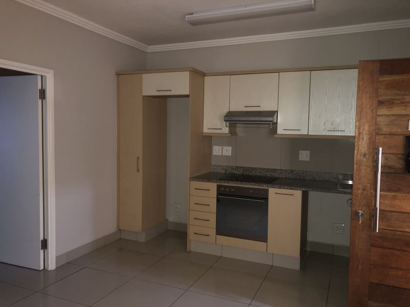 A compact kitchen featuring built-in cabinetry, granite countertops, an integrated oven and hob, and tiled flooring in a neutral, well-maintained space.