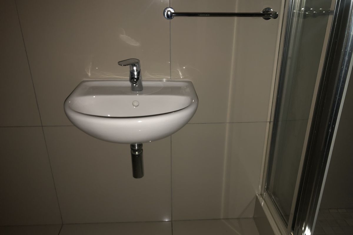 A clean, modern bathroom featuring a wall-mounted basin with chrome fixtures and a glass-enclosed shower area with neutral ceramic tiling.