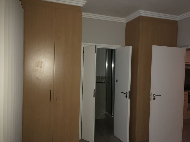A bedroom interior featuring built-in wooden cupboards and access to an adjoining bathroom area.