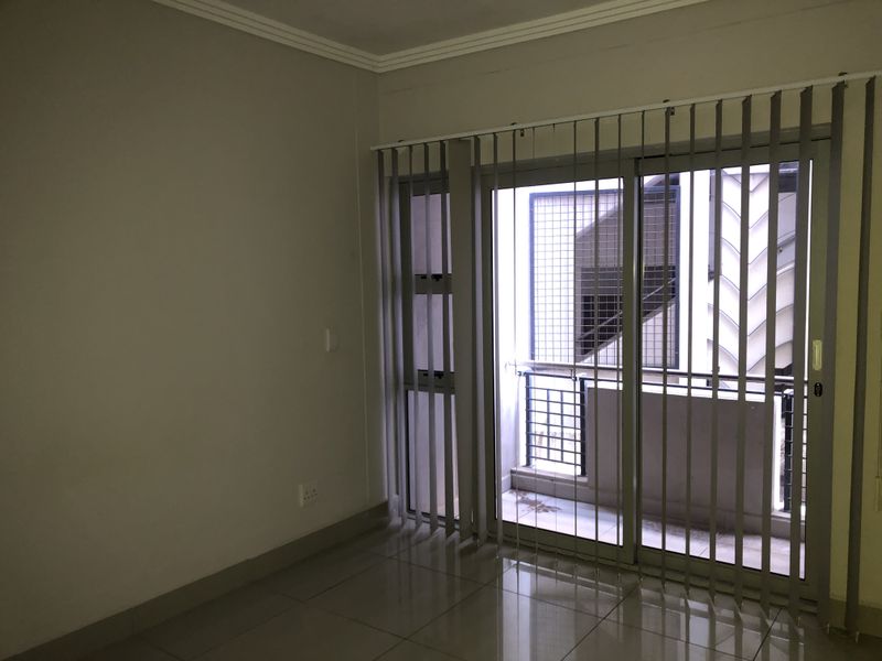 An empty living room featuring tiled flooring, coving, and a sliding glass door with integrated security gate leading to an outdoor area.