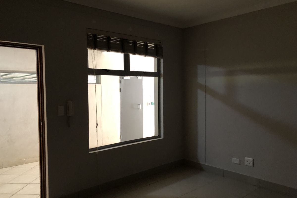 An empty bedroom featuring tiled flooring, neutral walls, and an aluminium window frame, offering a blank canvas for personalization.