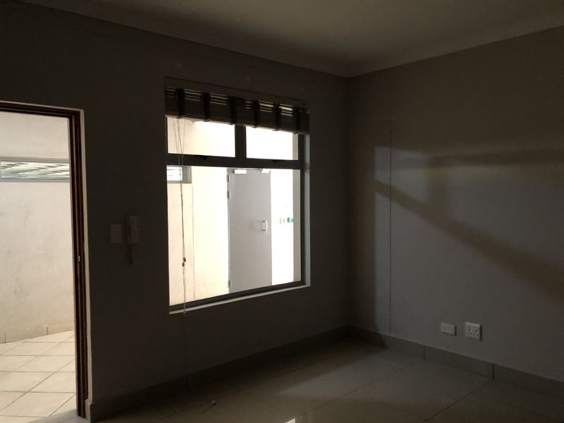 An empty bedroom featuring tiled flooring, neutral walls, and an aluminium window frame, offering a blank canvas for personalization.