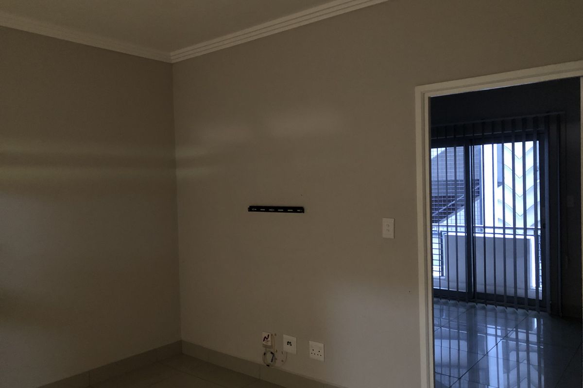 An empty living room featuring tiled flooring, crown molding, and a wall-mounted TV bracket, with a doorway leading to a balcony area.