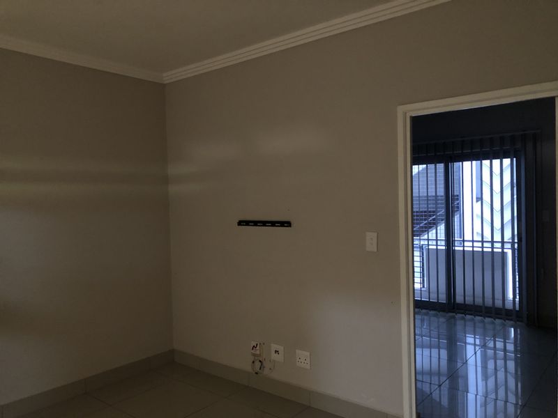 An empty living room featuring tiled flooring, crown molding, and a wall-mounted TV bracket, with a doorway leading to a balcony area.