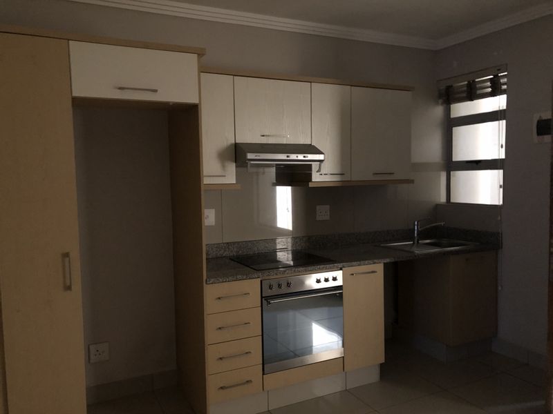 A functional kitchen featuring light wood cabinetry, granite countertops, a built-in oven, electric hob, and a stainless steel sink.