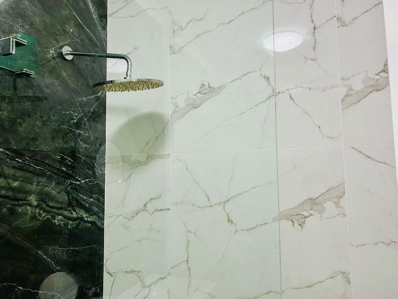A modern shower enclosure featuring high-contrast marble-effect wall tiling and a contemporary rainfall shower head.