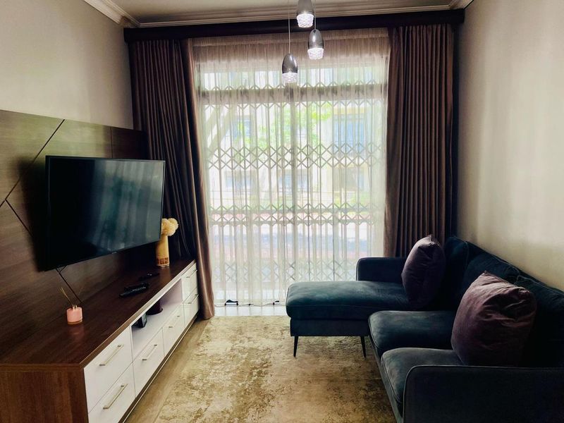 A cozy living room featuring a built-in media console, large window with security gate, and modern pendant lighting.