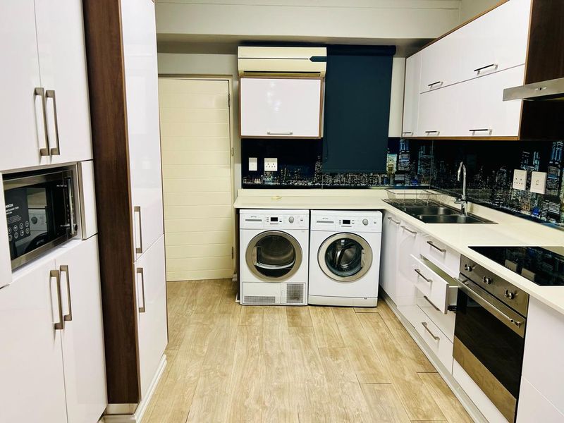 Modern kitchen featuring white high-gloss cabinetry, integrated appliances, built-in oven, hob, and a stylish city-scape splashback.