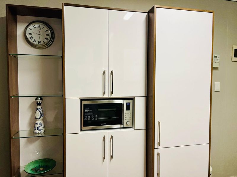 A modern kitchen wall unit featuring high-gloss white cabinetry, integrated microwave, and open glass shelving for display.