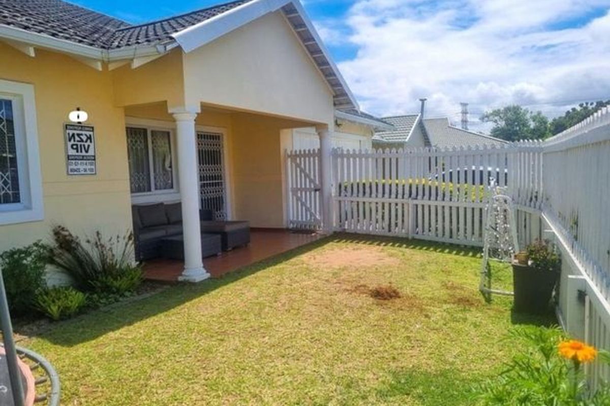 A rear view of the property featuring a covered patio area, tiled flooring, and a white picket fence enclosing a small garden space.