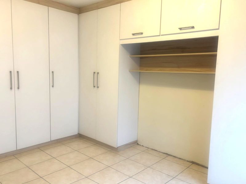 A clean, empty bedroom featuring white built-in cupboards with integrated shelving and neutral tiled flooring.