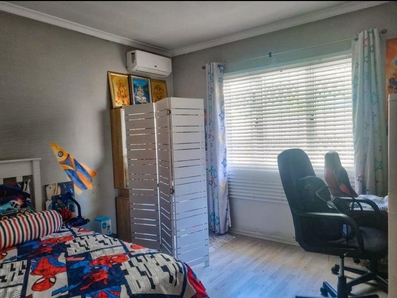 A bedroom featuring laminate flooring, a wall-mounted air conditioning unit, and venetian blinds, providing a functional space with neutral wall finishes.