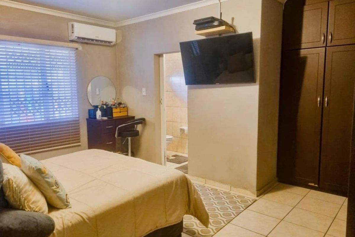 A functional bedroom featuring built-in cupboards, tiled flooring, an air conditioning unit, and direct access to an en-suite bathroom.