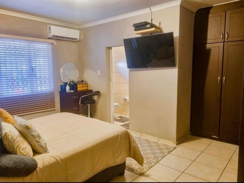 A functional bedroom featuring built-in cupboards, tiled flooring, an air conditioning unit, and direct access to an en-suite bathroom.