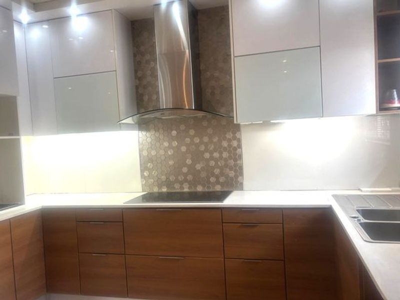 Modern kitchen featuring two-tone cabinetry, stainless steel extractor fan, hob, mosaic tile backsplash, and a double sink with integrated lighting.