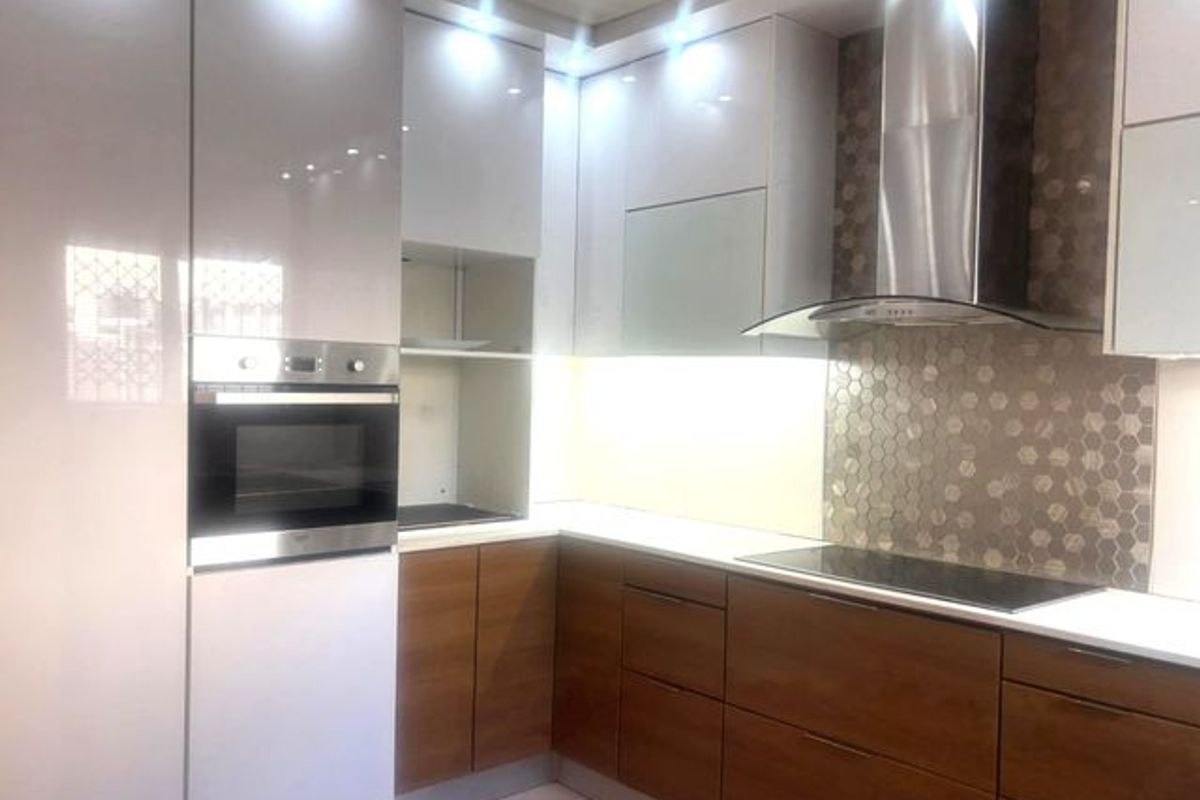 Modern kitchen featuring high-gloss cabinetry, built-in oven, integrated cooktop, stainless steel extractor fan, and a decorative hexagonal tiled backsplash.