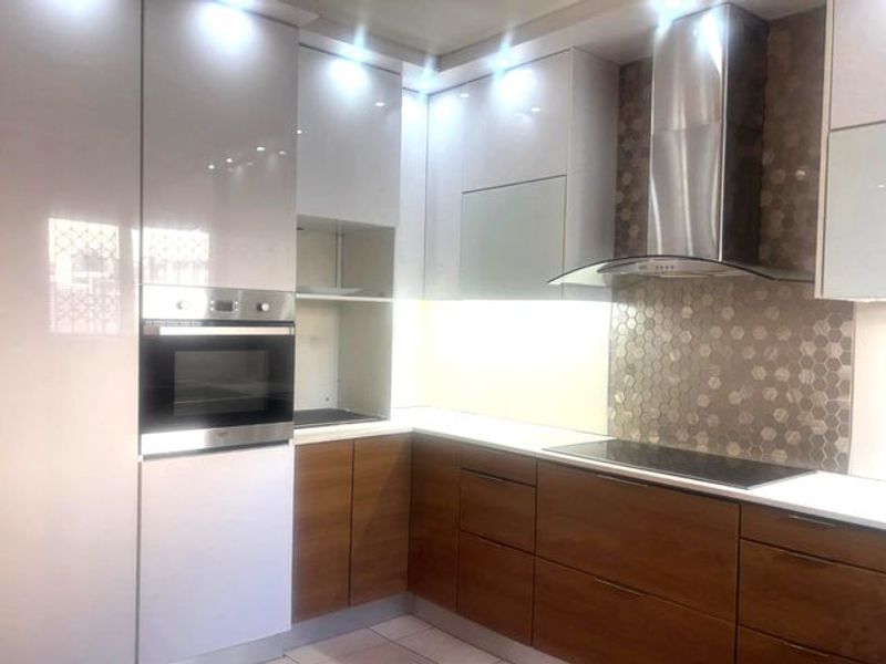 Modern kitchen featuring high-gloss cabinetry, built-in oven, integrated cooktop, stainless steel extractor fan, and a decorative hexagonal tiled backsplash.