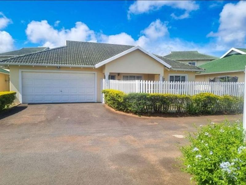 Front view of a well-maintained single-story house featuring a tiled roof, double garage, and a charming white picket fence with a paved driveway.