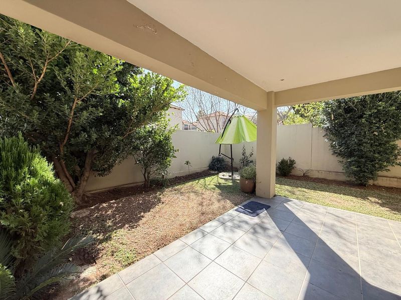 A covered patio area with tiled flooring, overlooking a private garden space enclosed by boundary walls.