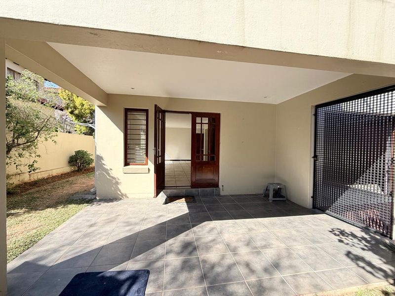 A covered patio area featuring tiled flooring, recessed lighting, and a timber-framed glass entrance door leading into the home.