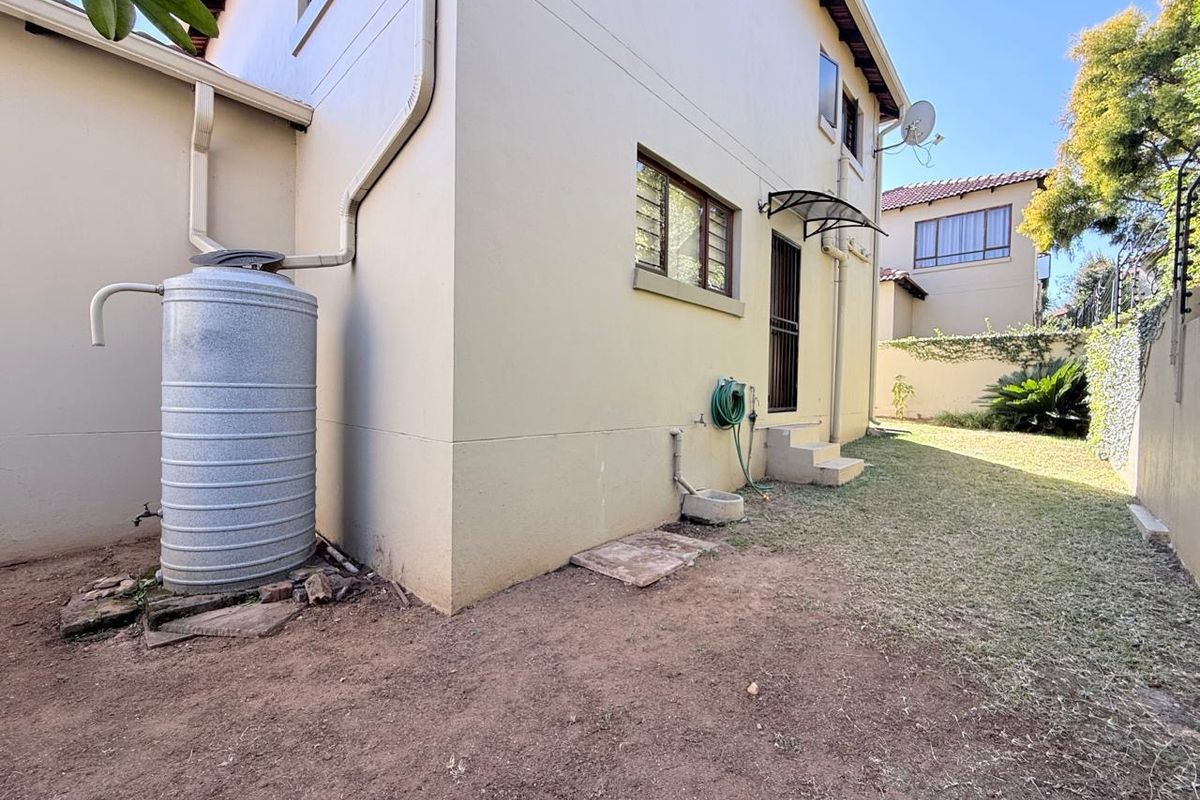 Rear exterior view of the property featuring a water tank, security gate, and a small garden area with boundary walling.