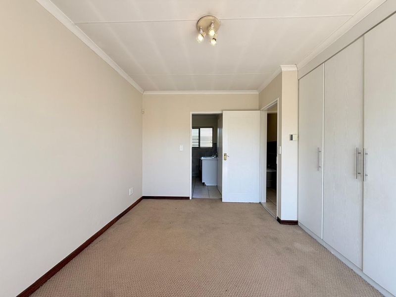 A vacant bedroom featuring built-in cupboards, neutral wall finishes, and carpeted flooring, with an adjacent doorway leading to a tiled utility or bathroom area.