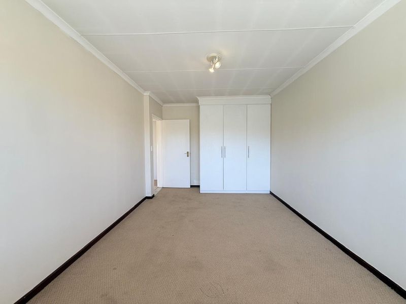 A clean, empty bedroom featuring neutral walls, carpeted flooring, and built-in white cupboards, offering a blank canvas for personalization.