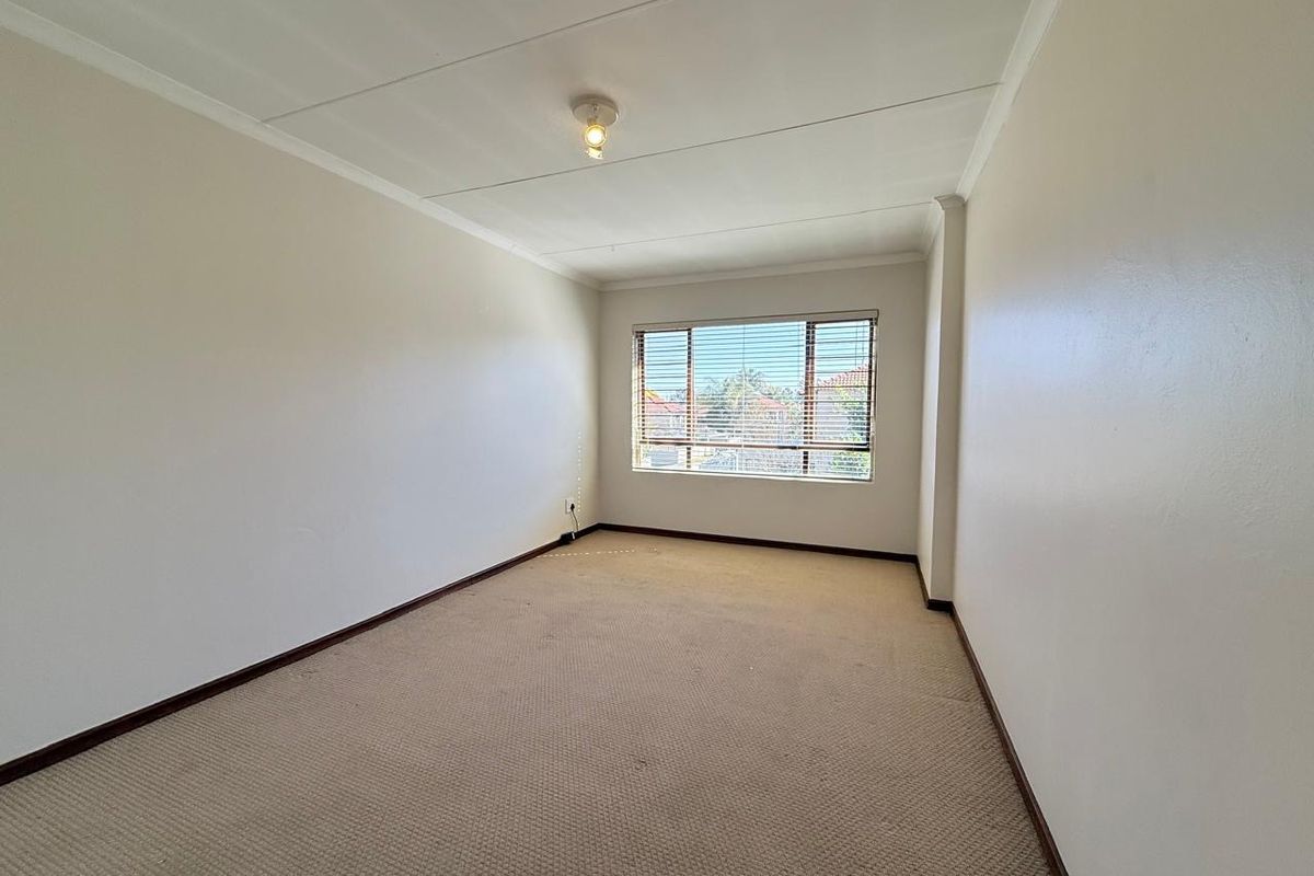 A spacious, empty bedroom featuring neutral walls, carpeted flooring, and a window fitted with venetian blinds.