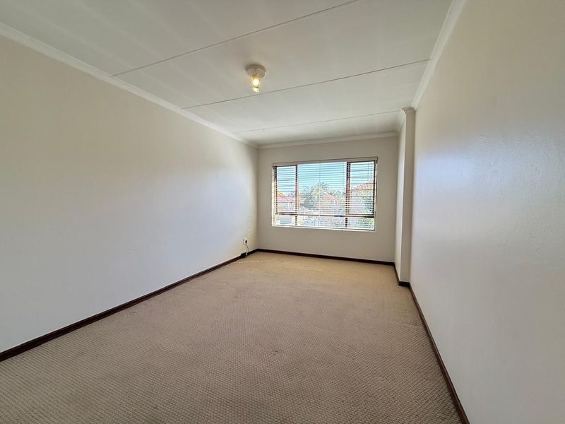 A spacious, empty bedroom featuring neutral walls, carpeted flooring, and a window fitted with venetian blinds.