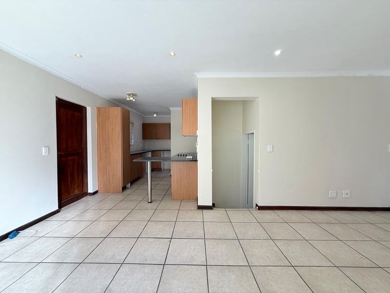An open-plan living and kitchen area featuring tiled flooring, built-in cabinetry, a breakfast counter, and direct access to a staircase.