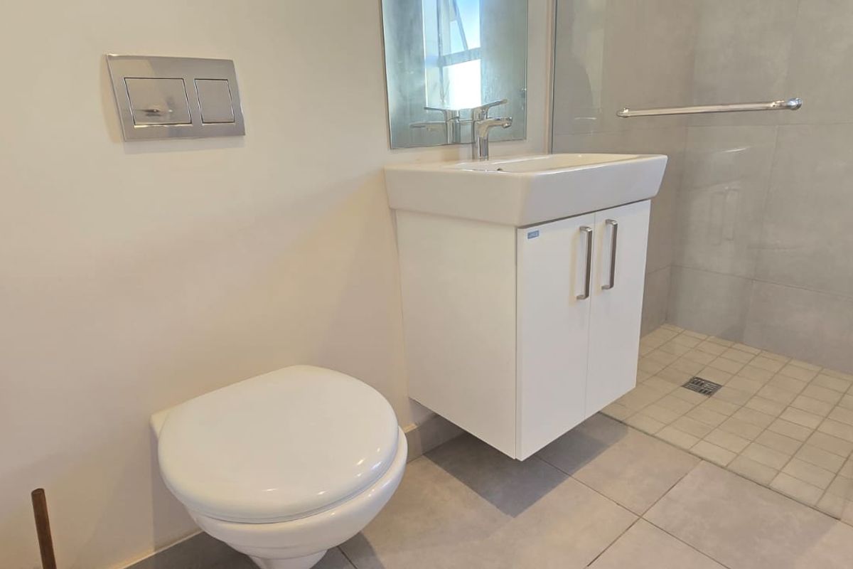 A modern, clean bathroom featuring a wall-hung toilet, vanity basin, and a walk-in shower with tiled finishes.
