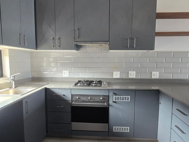 Modern kitchen featuring sleek grey cabinetry, subway tile backsplash, stone countertops, and integrated stainless steel appliances including a gas hob and oven.