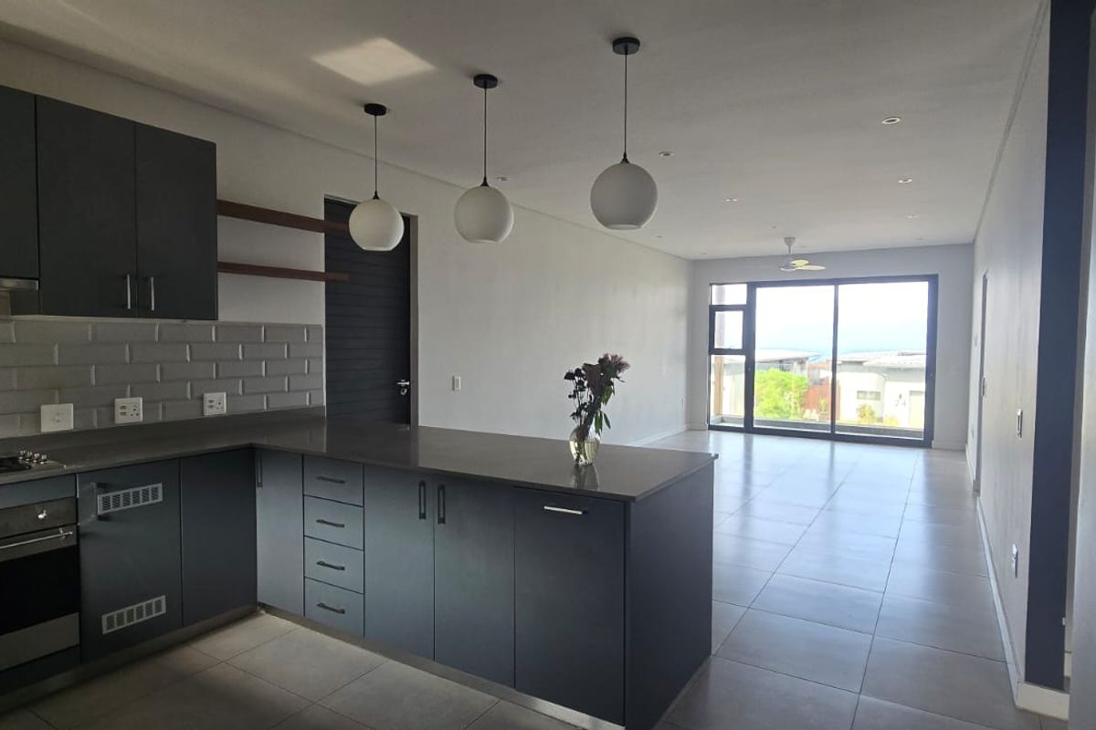 Modern open-plan kitchen and living area featuring dark cabinetry, stone countertops, subway tile backsplash, and large sliding doors leading to an outdoor space.