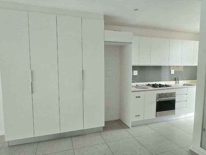 Modern kitchen featuring white built-in cabinetry, gas hob, integrated oven, and sleek tiled flooring in an open-plan layout.