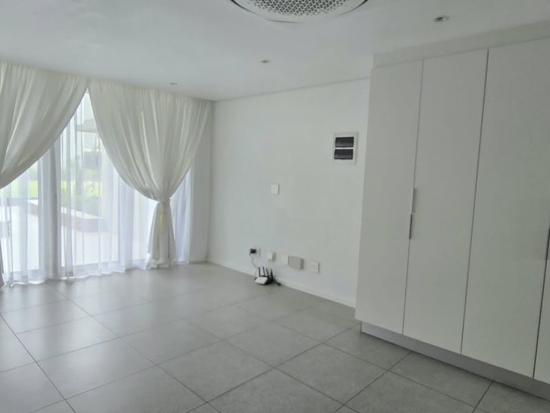 A bright, open-plan living area featuring neutral tiled flooring, built-in storage cupboards, and large sliding glass doors providing access to the exterior.