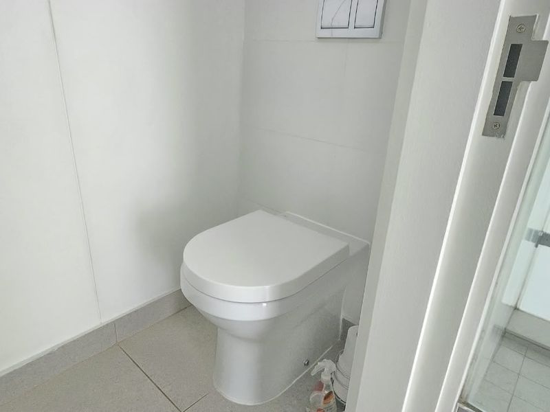 A clean and modern bathroom featuring a wall-hung toilet with a concealed cistern flush plate and neutral floor tiling.
