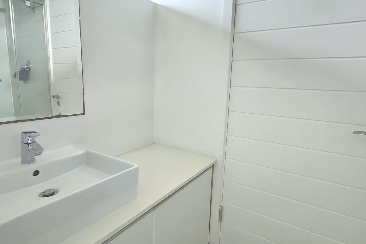 A clean, modern bathroom featuring a white countertop basin, vanity storage, wall-mounted mirror, and a glass-enclosed shower.