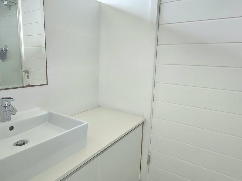 A clean, modern bathroom featuring a white countertop basin, vanity storage, wall-mounted mirror, and a glass-enclosed shower.