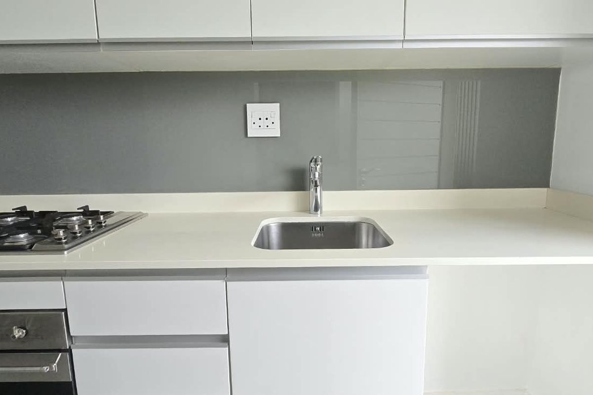 Modern kitchen area featuring white cabinetry, stone countertops, a gas hob, built-in oven, and a sleek glass splashback with a stainless steel sink.