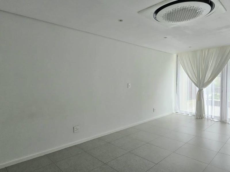 A bright, spacious, and empty living area featuring neutral tiled flooring, recessed lighting, a ceiling-mounted air conditioner, and large glass doors leading outdoors.